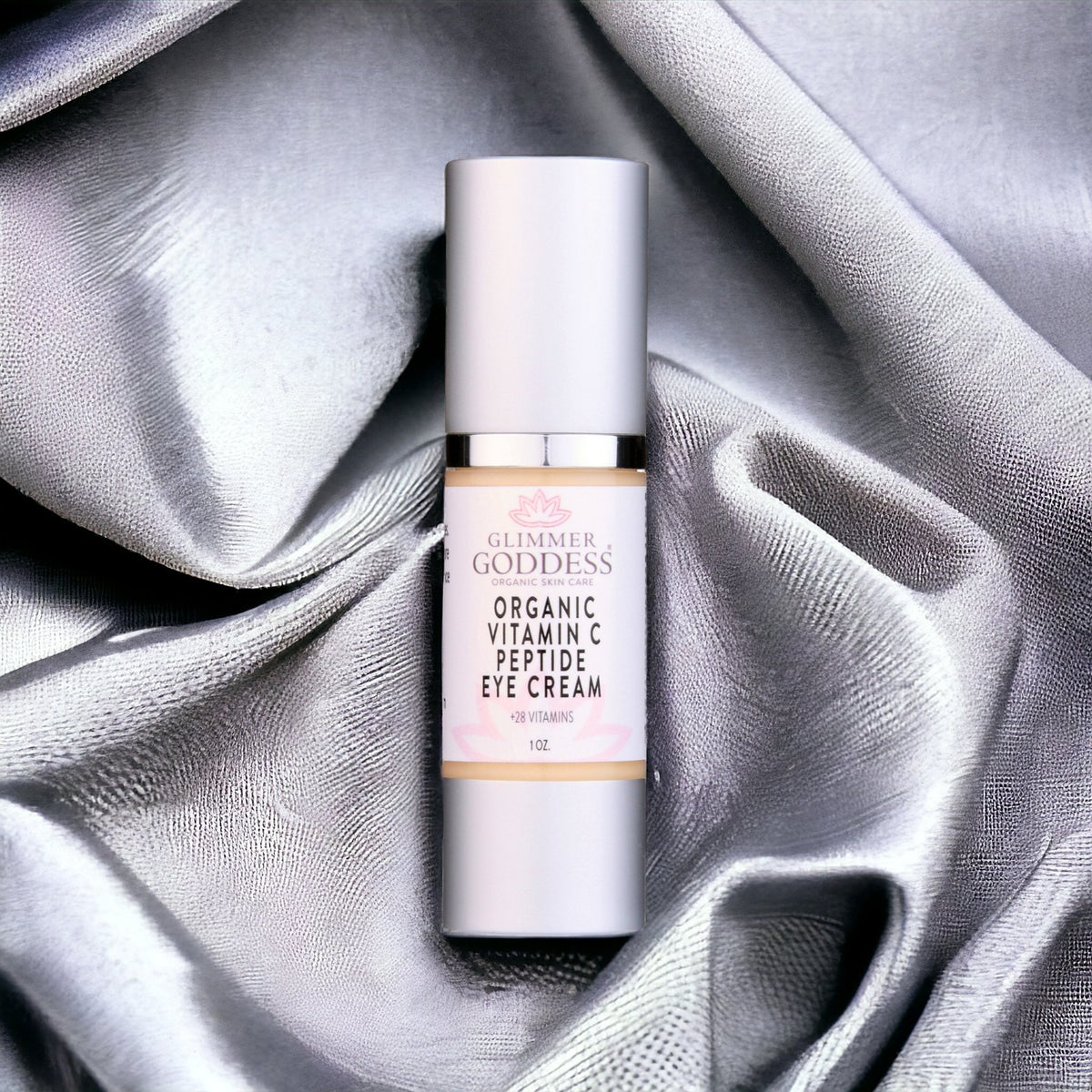 Organic Vitamin C Peptide Eye Cream in sleek bottle on silver fabric, nourishing skin care with 28 vitamins
