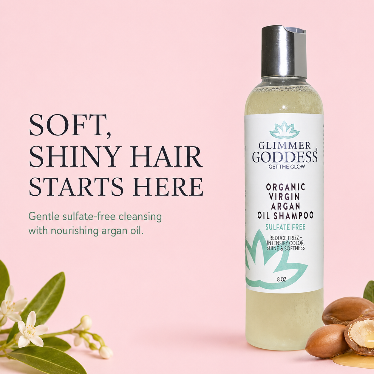 A bottle of Glimmer Goddess Organic Virgin Argan Oil Shampoo stands on a soft pink background with decorative leaves, flowers, and argan nuts. Large text on the left reads, 'SOFT, SHINY HAIR STARTS HERE.