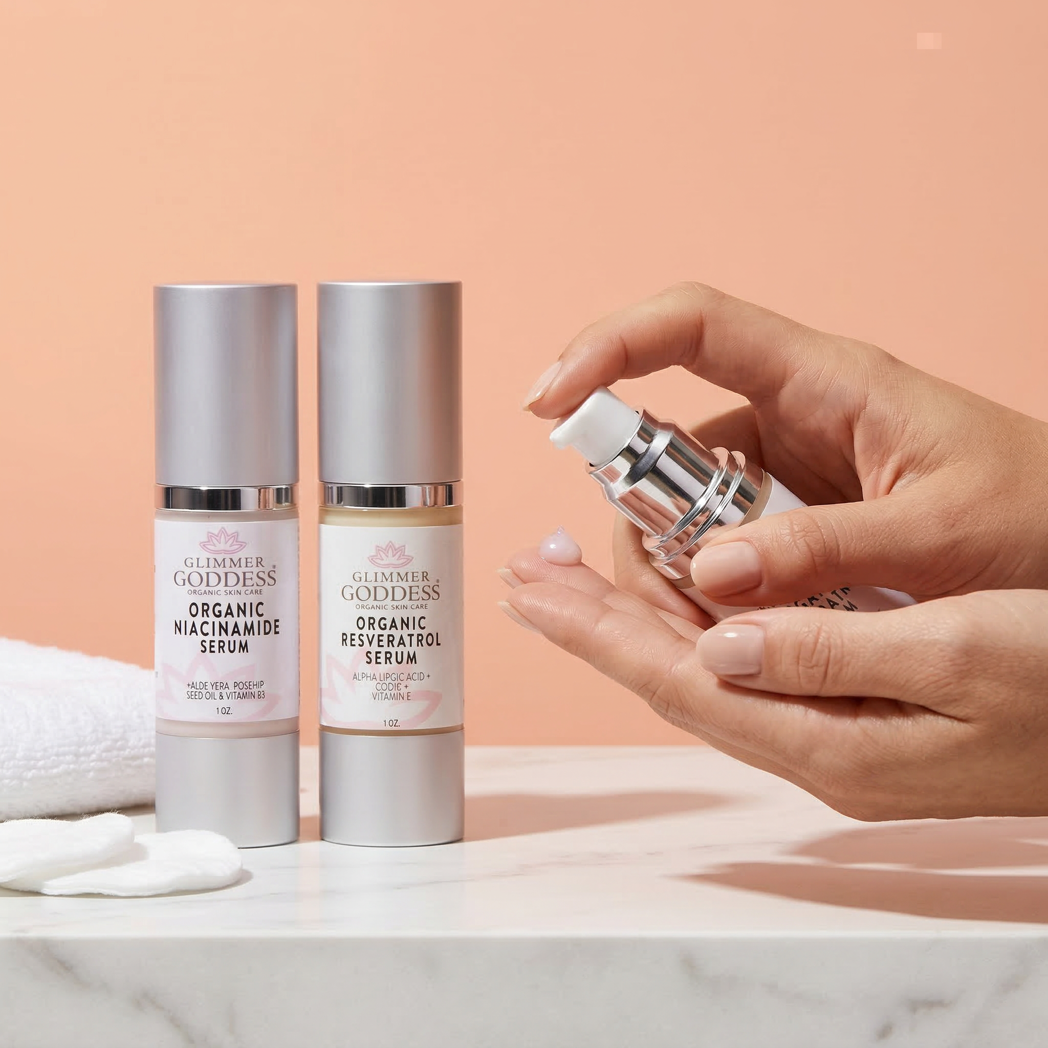Glimmer Goddess Organic Niacinamide + Resveratrol Serum Duo in a peach vanity scene, showing a hand dispensing serum from a matching frosted silver airless pump bottle, with both 1 oz serums visible for pore-minimizing, wrinkle-smoothing, and brightening skincare.