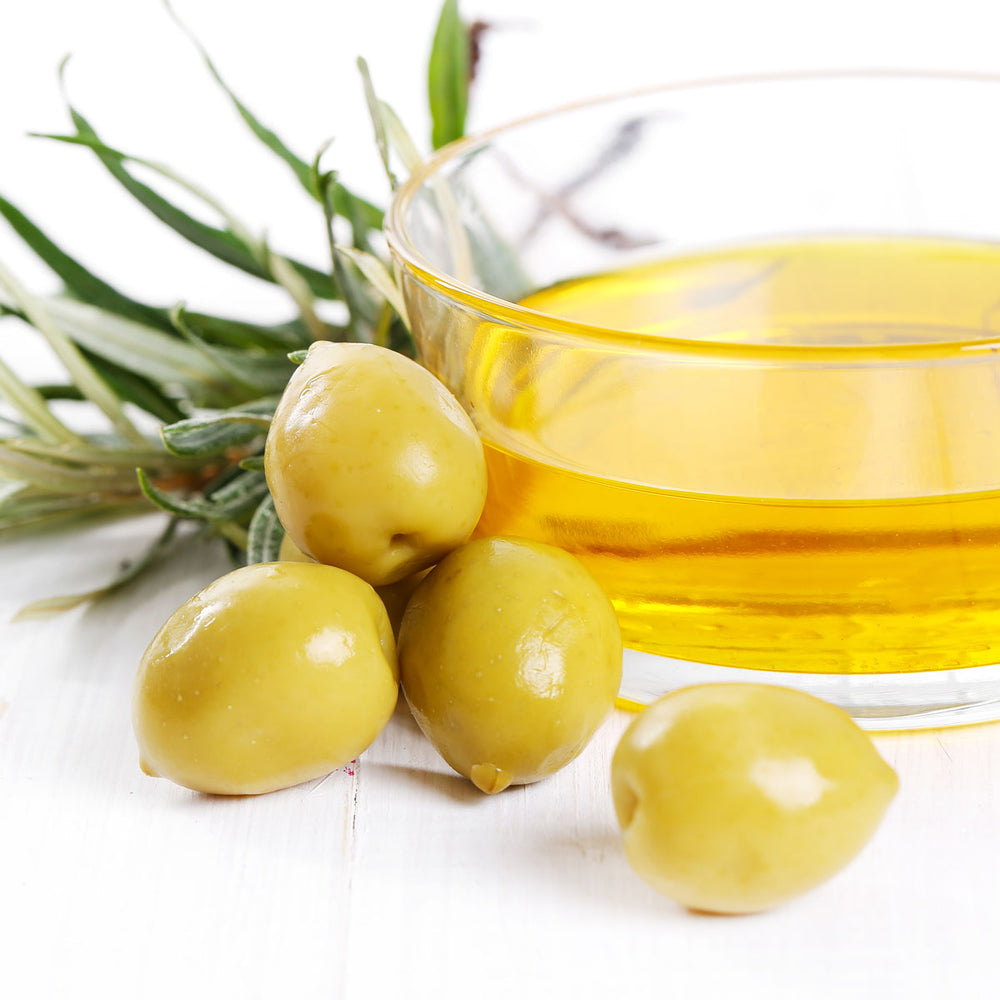 Bowl of olive oil with green olives and olive leaves on white background