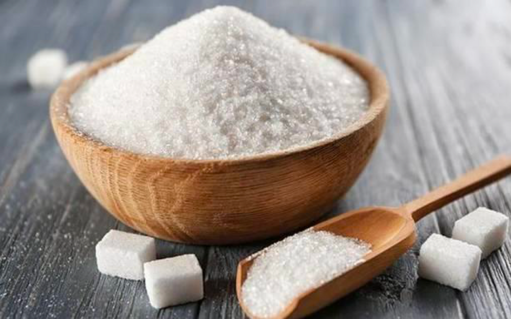 Granulated sugar in a wooden bowl with sugar cubes and a wooden spoon on a table